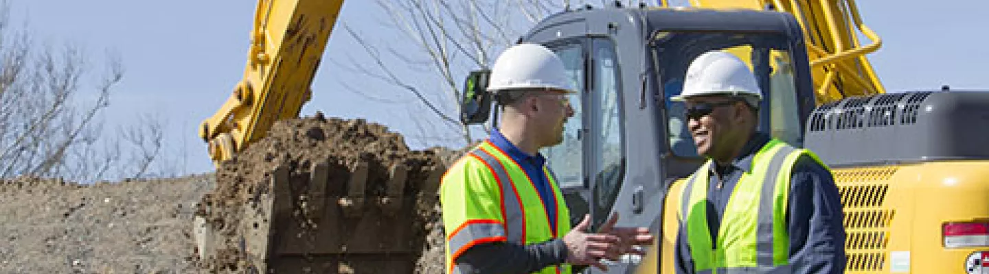 two men in hard hats on construction site with excavator 