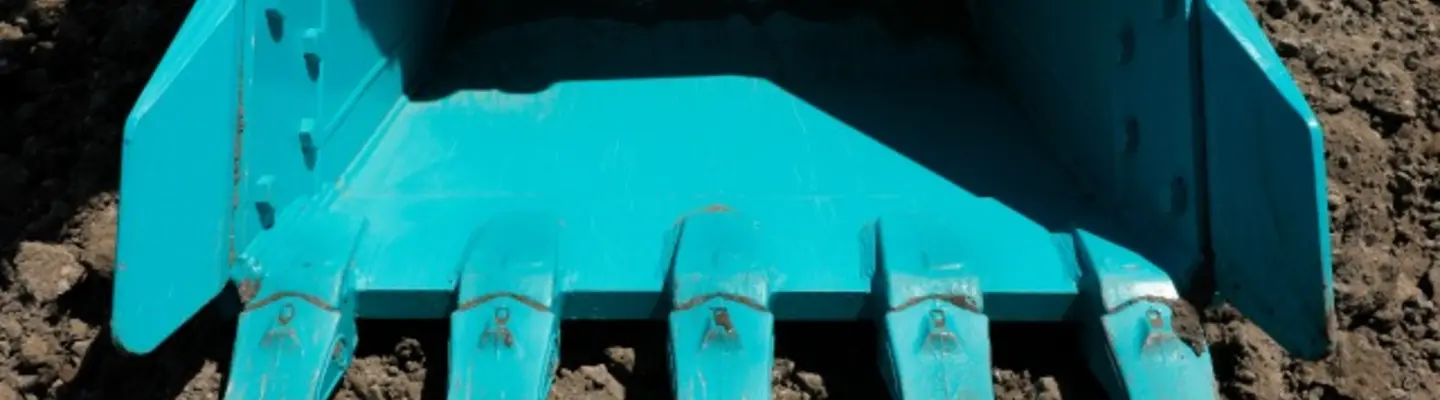 Bucket roller resting on sand at a construction site, used for compacting soil with safety barriers in the background.
