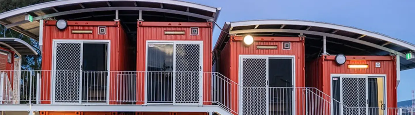 Two-story modular housing units made from shipping containers with exterior stairs and balconies at dusk.