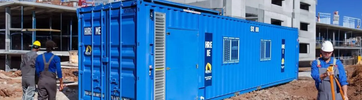 Blue shipping container office installed on a construction site with workers nearby.