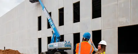 workers in safety vests looking at blue boom lift next to building