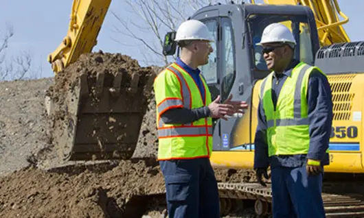 two men in hard hats on construction site with excavator 