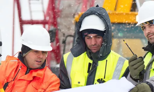 workers in safety vests and hard hats at a construction site in the winter
