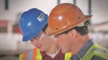 Two men in hard hats and safety vests talking