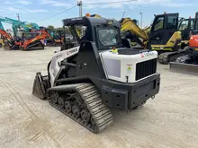 A truck loader attachment positioned on a construction site, ready for installation or use with heavy machinery.
