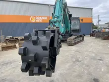 Compaction wheel attached to construction equipment, used for securing soil around newly installed safety barriers.